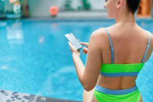 Mulher falando para o smartphone sentada na piscina representando automacao de piscina alexa